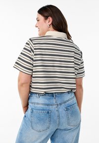 Chemise rayée en crème et noir, à manches courtes, coupe décontractée, assortie à un jean en denim bleu clair taille haute avec poches arrière.
