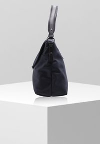 Granatowa nylonowa torba na ramię o uporządkowanej sylwetce, z teksturowanym paskiem i okrągłym akcentem z metalowego wykończenia. Szczegół z zamkiem błyskawicznym po boku.