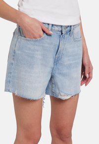 Shorts in denim azzurro con orlo sfilacciato, cinque tasche e chiusura con bottone classico. Il materiale è morbido e leggermente rovinato.