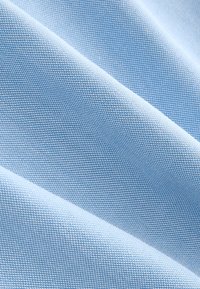 Tissu tissé bleu clair avec un motif texturé, présenté avec des plis doux créant des ombres et des reflets diagonaux.