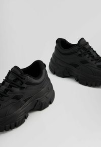 Czarne buty sportowe z fakturowaną cholewką, oddychającymi panelami z siateczki oraz masywną, wytrzymałą gumową podeszwą z wyraźnym bieżnikiem.