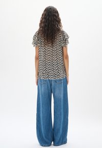 Top a fantasia nera e crema con maniche arricciate, abbinato a jeans in denim blu con vestibilità larga e tasche posteriori.