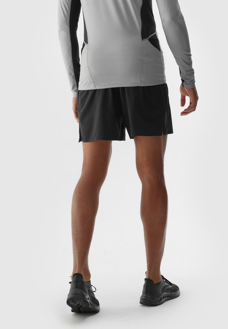 Strój sportowy składający się z jasnoszarej bluzki z długim rękawem z czarnymi akcentami oraz czarnych szortów, w połączeniu z czarnymi butami do biegania. Gładka tekstura.