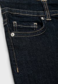 Tmavomodré džínsy s hladkou textúrou, viditeľným zlatým prešívaním a malým predným vreckom so strieborným kovovým gombíkom.