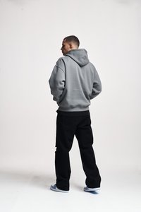 Gray hoodie with a large hood and loose fit, paired with black pants. The fabric appears soft, with ribbed cuffs and waistband. Blue sneakers.