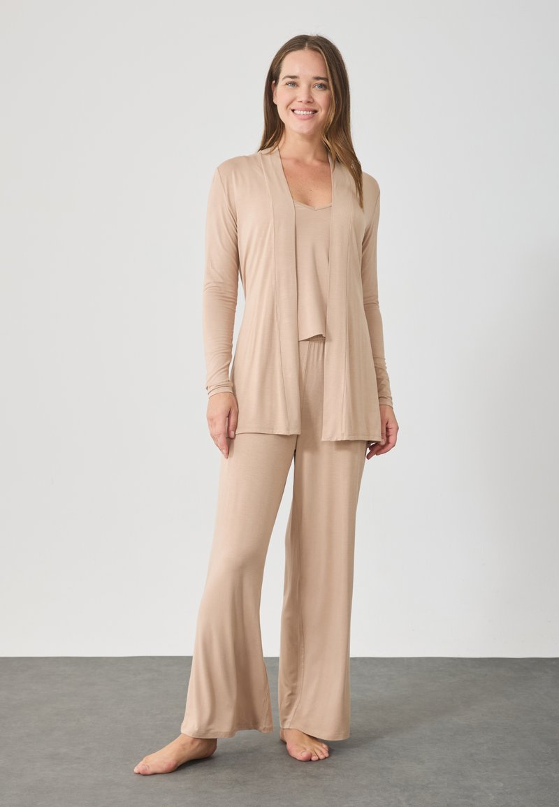 Μπεζ σετ καθιστικού που περιλαμβάνει ένα ανοιχτό μανίκι μακρύ cardigan, μια αμάνικη μπλούζα και καμπάνα παντελόνια φτιαγμένα από απαλό, ελαστικό ύφασμα με ομαλή υφή.