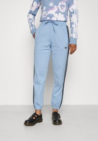 Light blue sweatpants with black side stripes, elastic waistband, and cuffed ankles, paired with a floral long-sleeve shirt and black shoes.