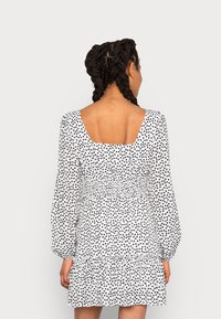 Vestido de estampado floral en blanco con lunares negros, con escote cuadrado, cintura fruncida y bajo con volantes. Mangas largas tipo globo.
