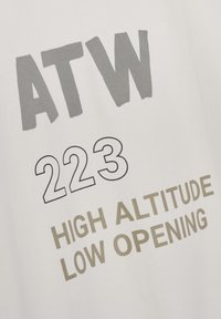 Witte T-shirt met gedurfde grijze tekst "ATW 223" en "HIGH ALTITUDE LOW OPENING", met een eenvoudig, strak ontwerp.