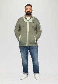 Light green knitted hoodie with contrasting light mint zippers, side pockets, and a hood, paired with blue jeans and white sneakers.