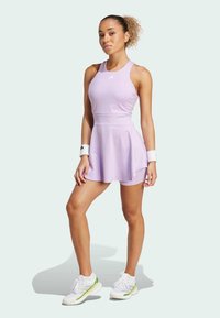 Light purple athletic dress with a fitted top and flared skirt, made of smooth fabric. White wristbands and green-accented sports shoes complete the look.