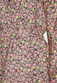Robe fleurie avec des fleurs roses et jaunes sur fond noir, avec une taille ceinturée et des manches bouffantes.