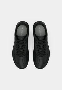 Μαύρα αθλητικά παπούτσια με λείο δέρμα στο επάνω μέρος, στρογγυλή μύτη, σχέδιο με κορδόνια και υφές. Η εσωτερική επένδυση εμφανίζει το λογότυπο της μάρκας.