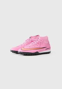 Pink soccer cleats with a high-top design, featuring black accents, textured surface, and a prominent orange Nike logo on the side.