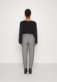 Haut transparent noir à manches longues avec un col rond, associé à un pantalon à carreaux gris doté d'une taille élastique et de poches latérales.