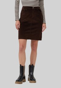 Leren bruine corduroy rok met een voorklepsluiting, twee zakken en knoopsluiting, gecombineerd met zwarte enkelboots met rubberen zolen en mesh-accenten.