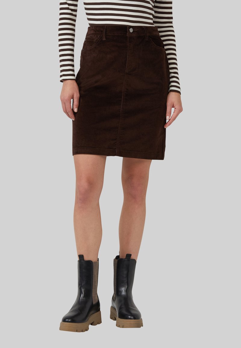 Leren bruine corduroy rok met een voorklepsluiting, twee zakken en knoopsluiting, gecombineerd met zwarte enkelboots met rubberen zolen en mesh-accenten.