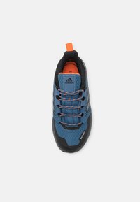 Zapatilla deportiva azul con parte superior de malla, suela negra y acentos naranjas. Presenta puntera reforzada, cordones y logotipo de la marca en la lengüeta.