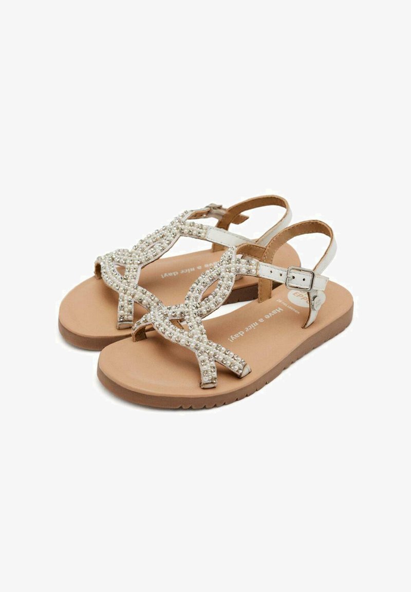 Las sandalias planas con cuentas presentan una suela beige, tirantes cruzados adornados con cuentas blancas y un hebilla en el tobillo para un ajuste seguro.