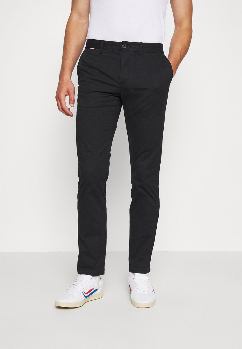 Svarta smala byxor av bomull med en slät textur. Har knappstängning, sidofickor och en röda och blå detalj på midjan.