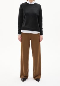 Pull noir à col rond, associé à un pantalon large marron. Textures lisses, design simple, et chaussures noires complètent le look.