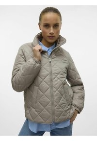 Gevoerde beige jas met een staande kraag, ritssluiting aan de voorkant en lange mouwen, gedragen over een blauwgestreept shirt. Zachte textuur, casual pasvorm.