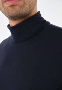 Pulover de tip guler înalt de culoare bleumarin, realizat dintr-un material moale, cu un design ajustat. Are o textură netedă și un guler înalt, potrivit pentru a fi purtat în straturi.