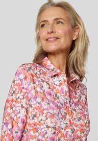 Bunte Bluse mit floralem Muster in Pink, Orange, Grau und Weiß. Mit Knopfleiste vorne, Kragen und glattem Stoff. 