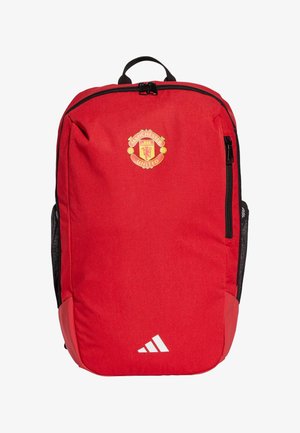 Sac à dos rouge avec le logo de Manchester United, poches latérales en maille noir, et rayures blanches Adidas en bas. Tissu durable, fermeture zippée.