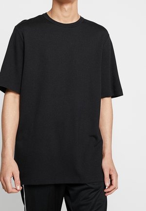 Camiseta negra de manga corta en un corte relajado, hecha de algodón suave, con un cuello redondo y una textura lisa, sin patrones ni gráficos.