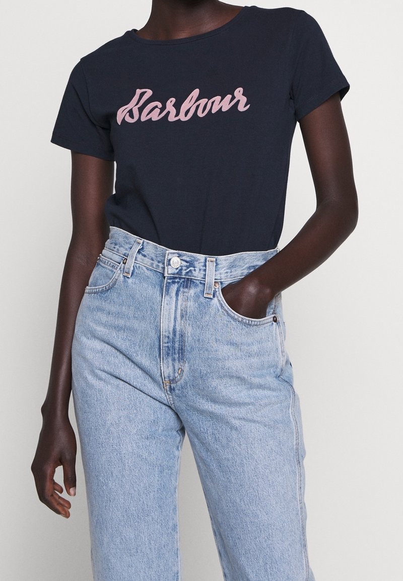 Námořnické bavlněné tričko s růžovým kurzivním logem "Barbour" v kombinaci s vysokými světle modrými džíny.