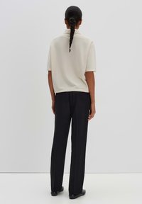 Polo shirt beige clair à manches courtes associé à un pantalon noir coupe droite ; le tissu semble lisse et la coupe est décontractée.