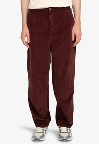 Maroon corduroy pants with a relaxed fit, featuring a button closure and front pockets. Textured fabric with vertical ridges.