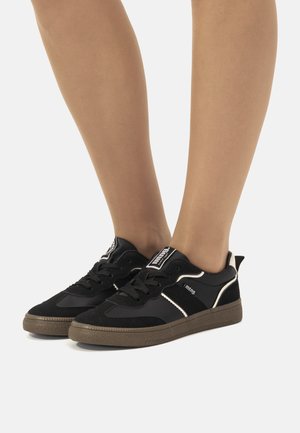 Zapatillas negras con una mezcla de ante y material sintético, que cuentan con una suela texturizada, acentos blancos y un logo negro en la lengüeta.