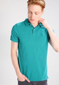 Polo shirt color teal realizzato in cotone, con colletto, due bottoni e un piccolo logo sul petto. Maniche corte e vestibilità dritta.