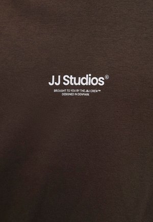 Weißes „JJ Studios“-Logo mit dem Text „Präsentiert vom J&J Team, entworfen in Dänemark“ auf braunem Stoffhintergrund.