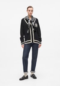 Cardigan negru cu dungi albe și închidere cu nasturi, asortat cu blugi închiși la culoare, o eșarfă argintie și pantofi slip-on negri cu ținte.