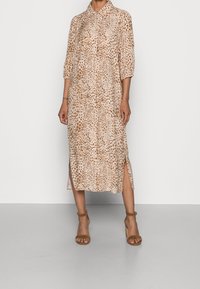 Abito midi caratterizzato da un tessuto beige con stampa leopardata marrone, davanti con bottoni, colletto e spacchi laterali. Indossato con tacchi a fascia marroni.