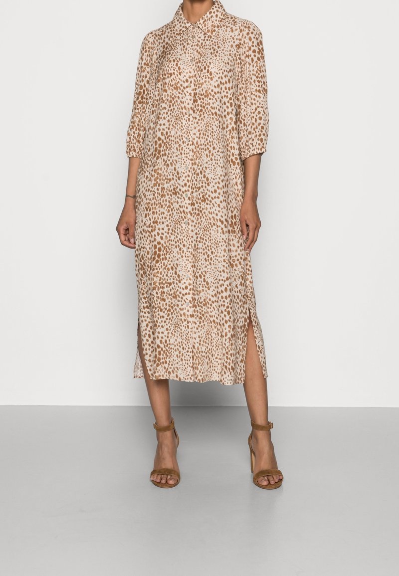 Abito midi caratterizzato da un tessuto beige con stampa leopardata marrone, davanti con bottoni, colletto e spacchi laterali. Indossato con tacchi a fascia marroni.