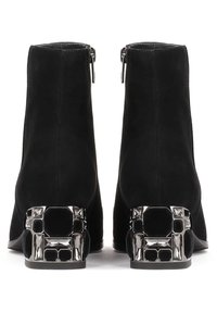 Botines de ante negros con un diseño elegante. Presentan un tacón bloque metálico decorativo con acentos geométricos y un cierre de cremallera en la parte trasera.
