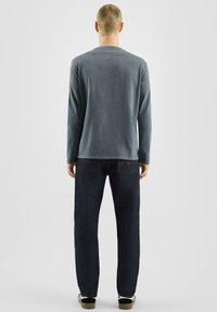 Langärmliges graues Shirt aus weichem Stoff, kombiniert mit dunkelblauen Jeans. Einfaches Design mit lockerer Passform und sichtbaren Nähten.