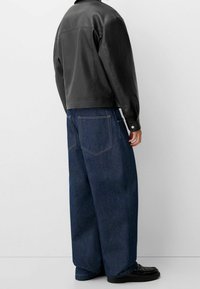 Zwarte leren jas met een getailleerde taille, gecombineerd met losse blauwe spijkerbroek met grote achterzakken en een gladde textuur.