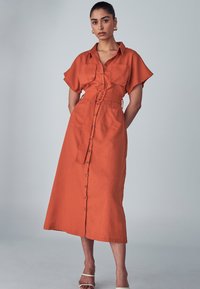 Orange button-up dress made of fabric with a slight texture. Features short sleeves, a belt at the waist, and two front pockets.