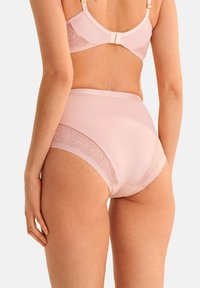 Culotte taille haute rose avec tissu lisse, accent en dentelle aux motifs circulaires, et design sans coutures pour plus de confort.