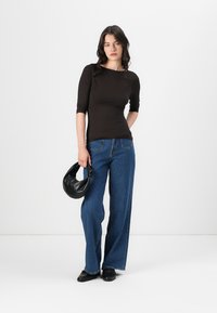 Svart tettsittende topp, blå vide bukser og en svart skinnveske. Glatt tekstur, med et enkelt design og nøytral fargepalett.