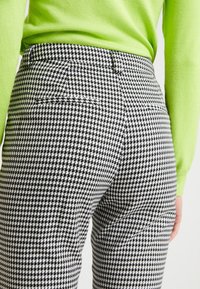 Detailní záběr osoby oblečené v černobílých kalhotách s houndstooth vzorem a jasně zeleném dlouhém tričku, zobrazeno zezadu od pasu dolů.