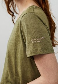 Olivgrön, kortärmad t-shirt gjord av mjukt tyg, med broderad text "solen är alltid i mitt hjärta" på vänster ärm.