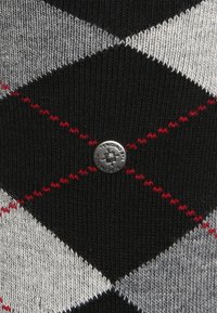 Suéter de punto con un patrón que presenta formas de diamante en negro, gris y blanco con acentos rojos, y un botón de logo metálico en el centro.