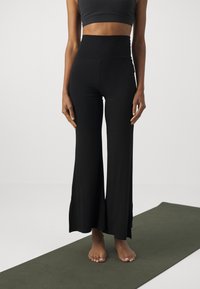 Black high-waisted flared yoga pants made of smooth, stretchy fabric, featuring wide legs and a seamless waistband.