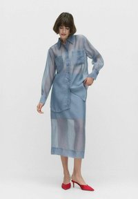 Vaaleansininen, läpikuultava nappipaita, jossa on tasku, yhdistettynä matching-hameeseen. Pitkät hihat ja sileä rakenne. Punaiset korkokengät.